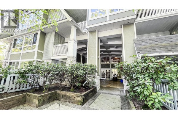 Pathway leading to apartment building entrance with decorative paving and planters. - 306 1111 Lynn Valley Road, North Vancouver