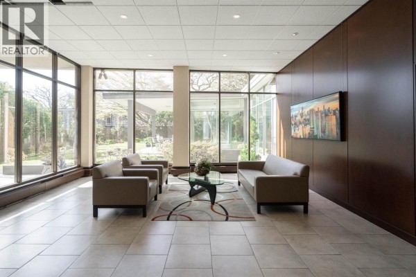 Building lobby with beige tile floors, glass walls, and a seating area with sofas. - 306 2055 Pendrell Street, Vancouver