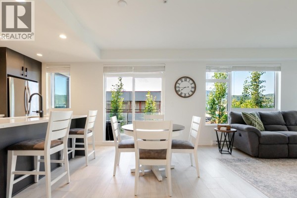 Living and dining area with white table, grey couch, and large windows. - 306 3018 St. George Street, Port Moody