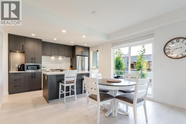 Dining area with white table and chairs next to a modern kitchen. - 306 3018 St. George Street, Port Moody