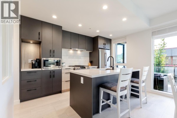 Modern kitchen with dark cabinets, white countertops, and stainless steel appliances. - 306 3018 St. George Street, Port Moody