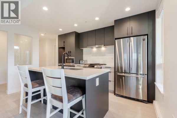 Kitchen island with bar stools, dark cabinets, and stainless steel refrigerator. - 306 3018 St. George Street, Port Moody