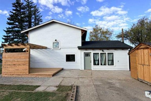 Rear exterior of the white house with a wooden deck and a detached wooden shed. - 306 47 Avenue W, Claresholm