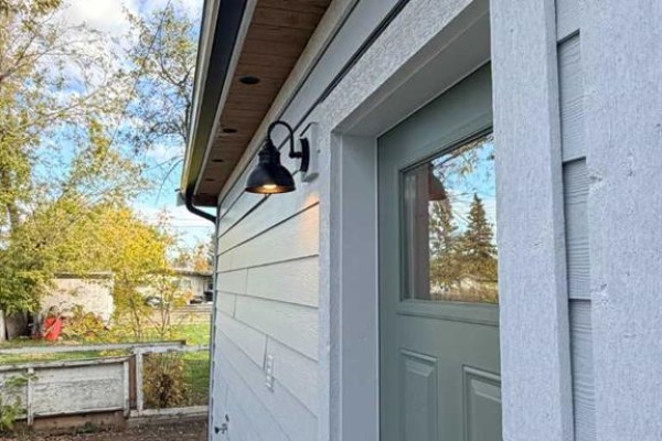 Close-up of a black outdoor light fixture mounted on a white siding wall near a light green door. - 306 47 Avenue W, Claresholm