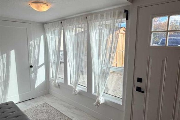 Interior view of a bright sunlit room with white sheer curtains covering three windows. - 306 47 Avenue W, Claresholm
