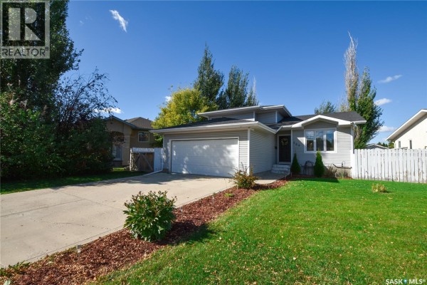 Exterior view of the house from the side with green lawn and mature trees. - 306 O'regan Crescent, Saskatoon