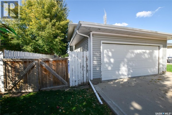 Close-up of the garage door, wooden gate, and white picket fence in the backyard. - 306 O'regan Crescent, Saskatoon
