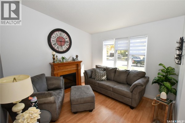 Living room with two grey sofas, fireplace, ottoman, and large wall clock. - 306 O'regan Crescent, Saskatoon