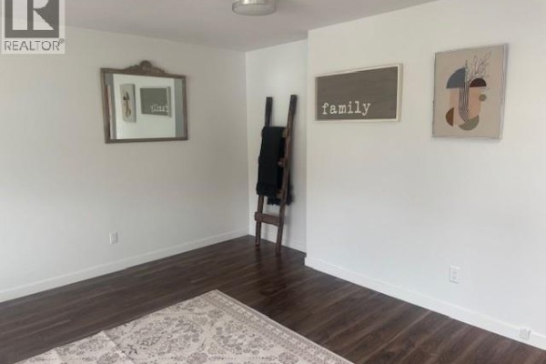 A bathroom vanity with wooden cabinets, countertop, sink, mirror, and a toilet. - 3065 Wilson Street Unit# 108, Penticton