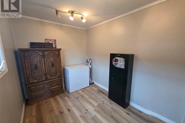 Interior room with wooden floors, a large wooden cabinet, a white freezer, and a black safe. - 3069 Walsh River Road, Labrador City