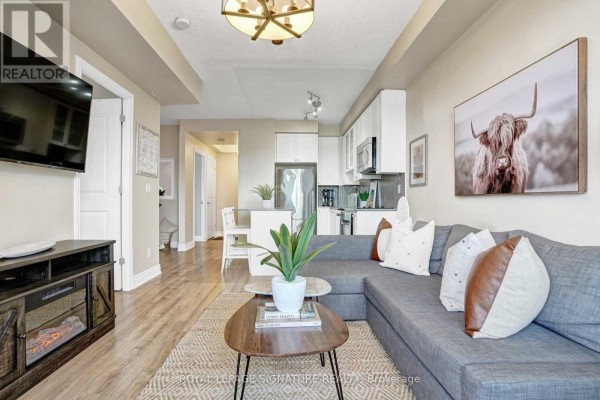 Living room and kitchen area with a sectional sofa, coffee table, and view to hallway. - 306a - 9088 Yonge Street, Richmond Hill
