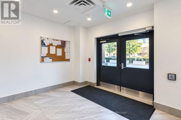 Building lobby entrance with double doors, bulletin board, and emergency exit sign. - 307 - 1 Wellington Street, Brantford