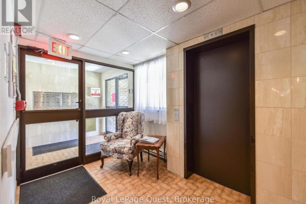 Apartment building interior hallway with mailboxes, chair, and elevator. - 307 - 1047 Mississaga Street W, Orillia