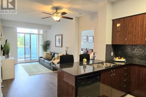 Living room with sofa and balcony access, adjacent to a dark granite kitchen island. - 307 - 5791 Yonge Street, Toronto