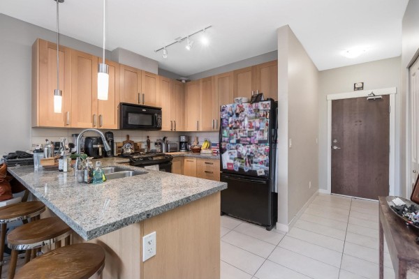 Kitchen with light wood cabinets, granite island, and black appliances, adjacent to a hallway. - 307 15918 26 Avenue, Surrey