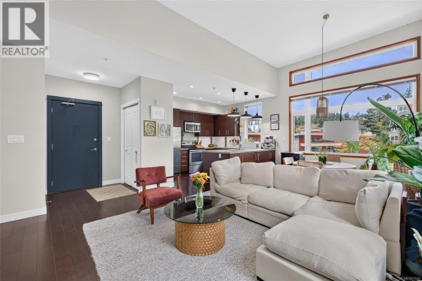 Living room with a dark blue front door, white sectional sofa, and dark wood kitchen cabinets. - 307 170 Nursery Hill Dr, View Royal