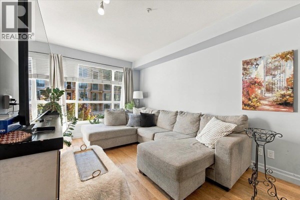 Living room featuring a sectional sofa, fireplace, and a window with a view of adjacent buildings. - 307 2343 Atkins Avenue, Port Coquitlam