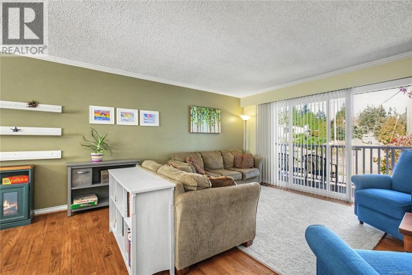 Living room with a sofa, blue armchair, fireplace, and sliding glass doors. - 3071 Shamrock Pl, Nanaimo