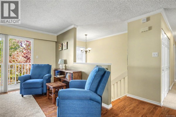 Living room with two blue armchairs, a wooden table, and a bookshelf. - 3071 Shamrock Pl, Nanaimo