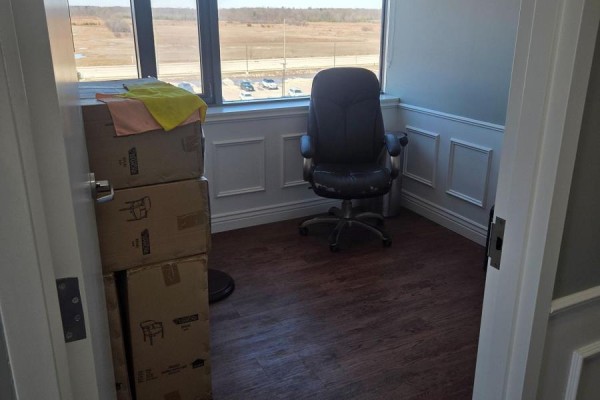An empty office with a leather chair, stacked boxes, and a window overlooking a parking lot. - 3075 Hospital Gate, Oakville