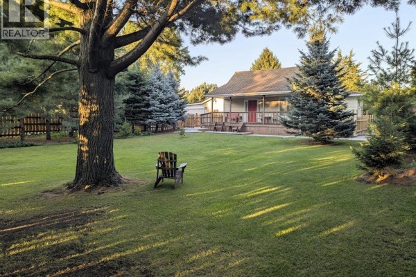 Lush green lawn with a wooden Adirondack chair in front of a light yellow house with a deck. - 30759 Cairo Road, Bothwell