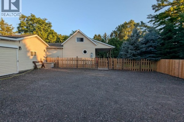 View of the garage, light yellow house, and a wooden fence enclosing the backyard area. - 30759 Cairo Road, Bothwell
