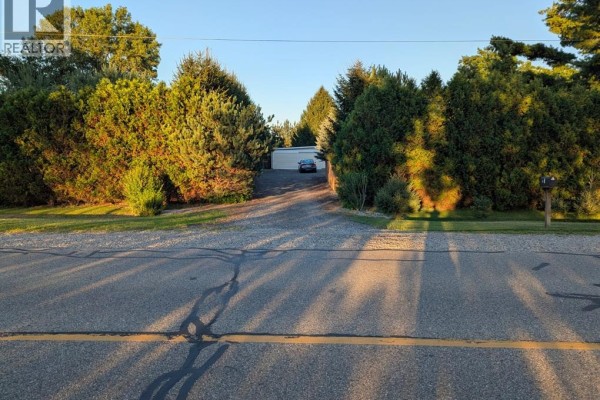 View from the street looking up a long driveway towards a house and garage surrounded by trees. - 30759 Cairo Road, Bothwell