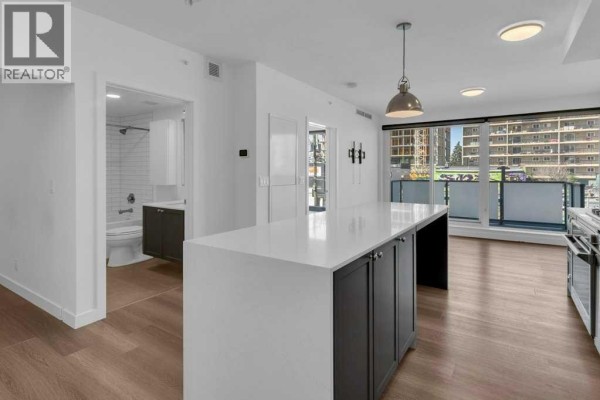 Open concept living area with a white island, dark cabinets, and a view. - 308, 327 9a Street Nw, Calgary