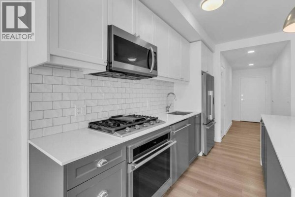 Modern kitchen with white subway tile backsplash, stainless steel appliances, and grey cabinets. - 308, 327 9a Street Nw, Calgary