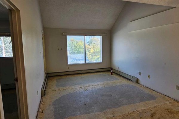 Empty room with sloped ceiling, large window, and exposed subfloor. - 308, 5015 51 St Street, Taber