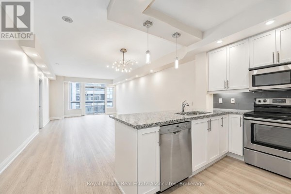 Open concept kitchen and living area with white cabinets, granite island, and stainless steel appliances. - 308 - 1 Hurontario Street, Mississauga