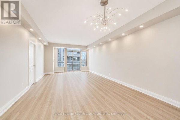 Spacious living room with light wood floors, recessed lighting, and large windows with a city view. - 308 - 1 Hurontario Street, Mississauga