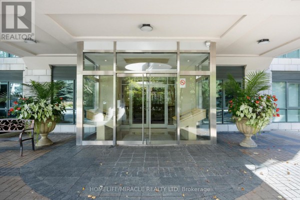 Front entrance with double glass doors, flanked by large potted plants and stone paving. - 308 - 11 William Carson Crescent, Toronto