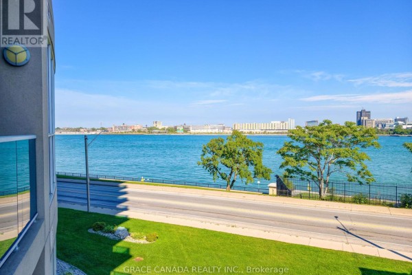 View of the river and city skyline from an apartment balcony with green lawn. - 308 - 1225 Riverside Drive W, Windsor