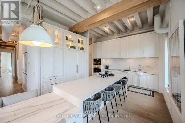 White modern kitchen with island, bar stools, marble countertops, and built-in appliances. - 308 - 19 Guelph Avenue, Cambridge