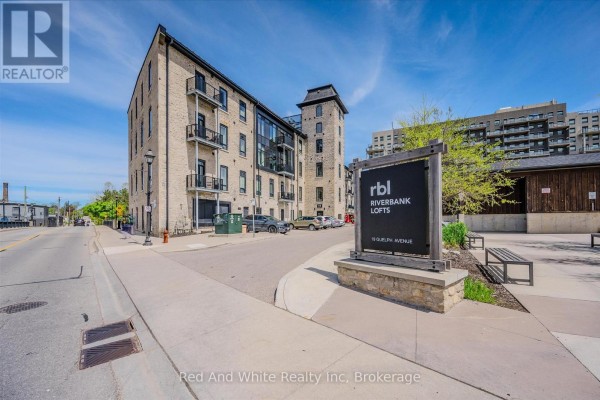 Exterior view of a historic brick building with many windows next to a river and waterfall. - 308 - 19 Guelph Avenue, Cambridge