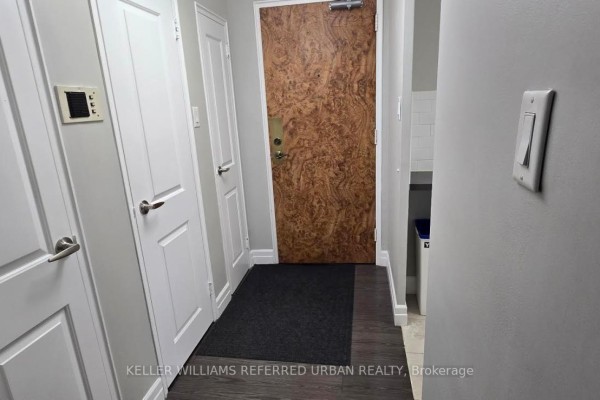 Apartment entryway with a wood veneer door, dark grey mat, white doors, and light grey walls. - 308 - 1901 Bayview Avenue, Toronto