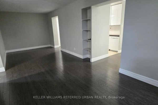 Apartment living room with dark hardwood floors, light grey walls, and an open doorway to the kitchen. - 308 - 1901 Bayview Avenue, Toronto