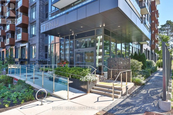Building entrance with glass doors, ramp, and landscaped greenery. - 308 - 21 Park Street E, Mississauga