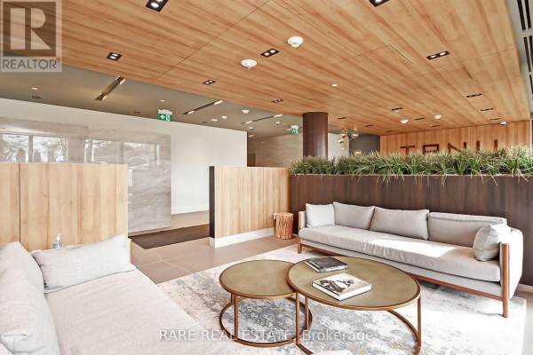 Lobby seating area with light grey sofas, coffee tables, and wood paneling. - 308 - 21 Park Street E, Mississauga