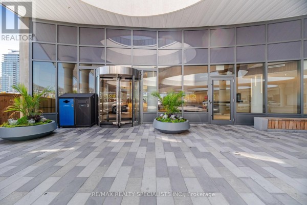Glass revolving doors and entrance to modern building with potted plants and tiled walkway. - 308 - 5105 Hurontario Street, Mississauga
