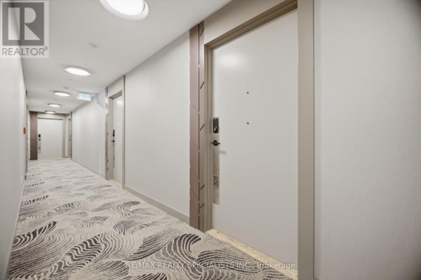 Long apartment building hallway with patterned carpet, several doors, and overhead lighting. - 308 - 5105 Hurontario Street, Mississauga