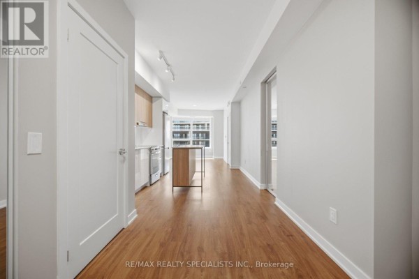 Interior hallway view towards an open concept kitchen with wood floors and light walls. - 308 - 5105 Hurontario Street, Mississauga