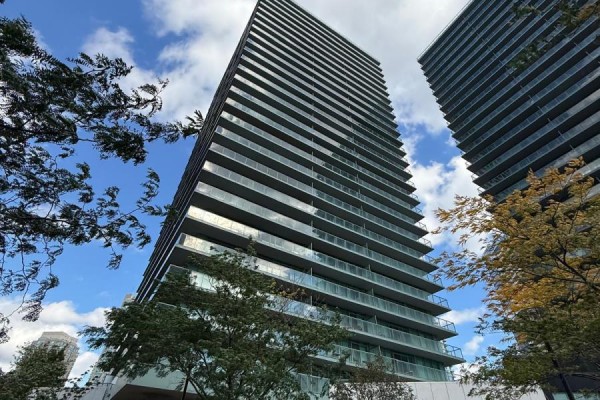View from below of a tall apartment building with glass balconies against a blue sky. - 308 - 5508 Yonge Street Ne, Toronto