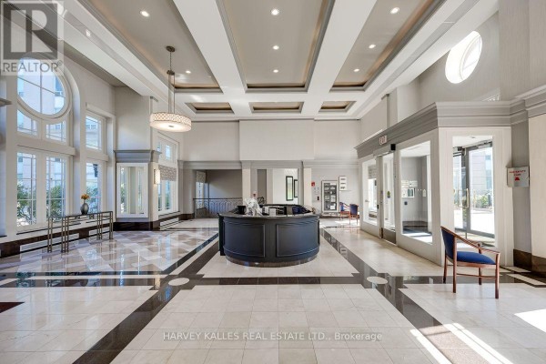 Building lobby with a central dark wood reception desk, marble floors, and large windows. - 308 - 8 Covington Road, Toronto