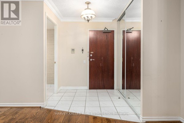 Apartment entryway with white tiled floor, dark wood door, and mirrored closet. - 308 - 8 Covington Road, Toronto