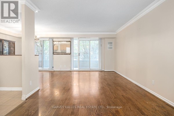Living and dining area with dark wood floors, beige walls, and sliding glass doors. - 308 - 8 Covington Road, Toronto