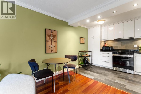 Kitchen area with white cabinets, stainless steel appliances, and a small dining table with chairs. - 308 2040 Cornwall Avenue, Vancouver