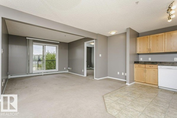 Living room with beige carpet, grey walls, and a sliding glass door to a balcony. - #308 309 Clareview Station Dr Nw, Edmonton