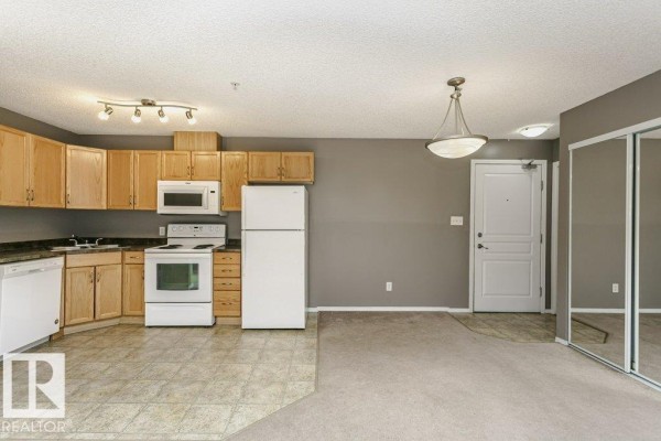 Kitchen area with light wood cabinets, white appliances, and beige tiled flooring. - #308 309 Clareview Station Dr Nw, Edmonton